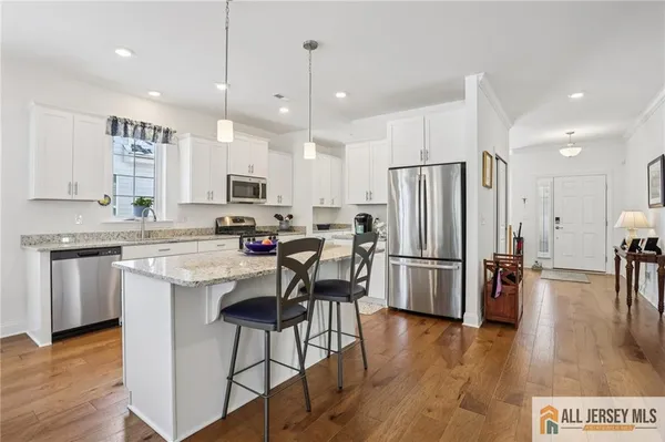 a kitchen with stainless steel appliances granite countertop a refrigerator a stove a sink a dining table and chairs with wooden floor