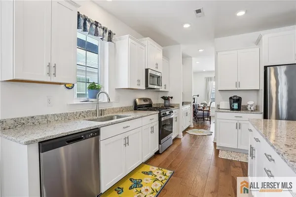 a kitchen with stainless steel appliances granite countertop a sink a stove a refrigerator and island with wooden floor