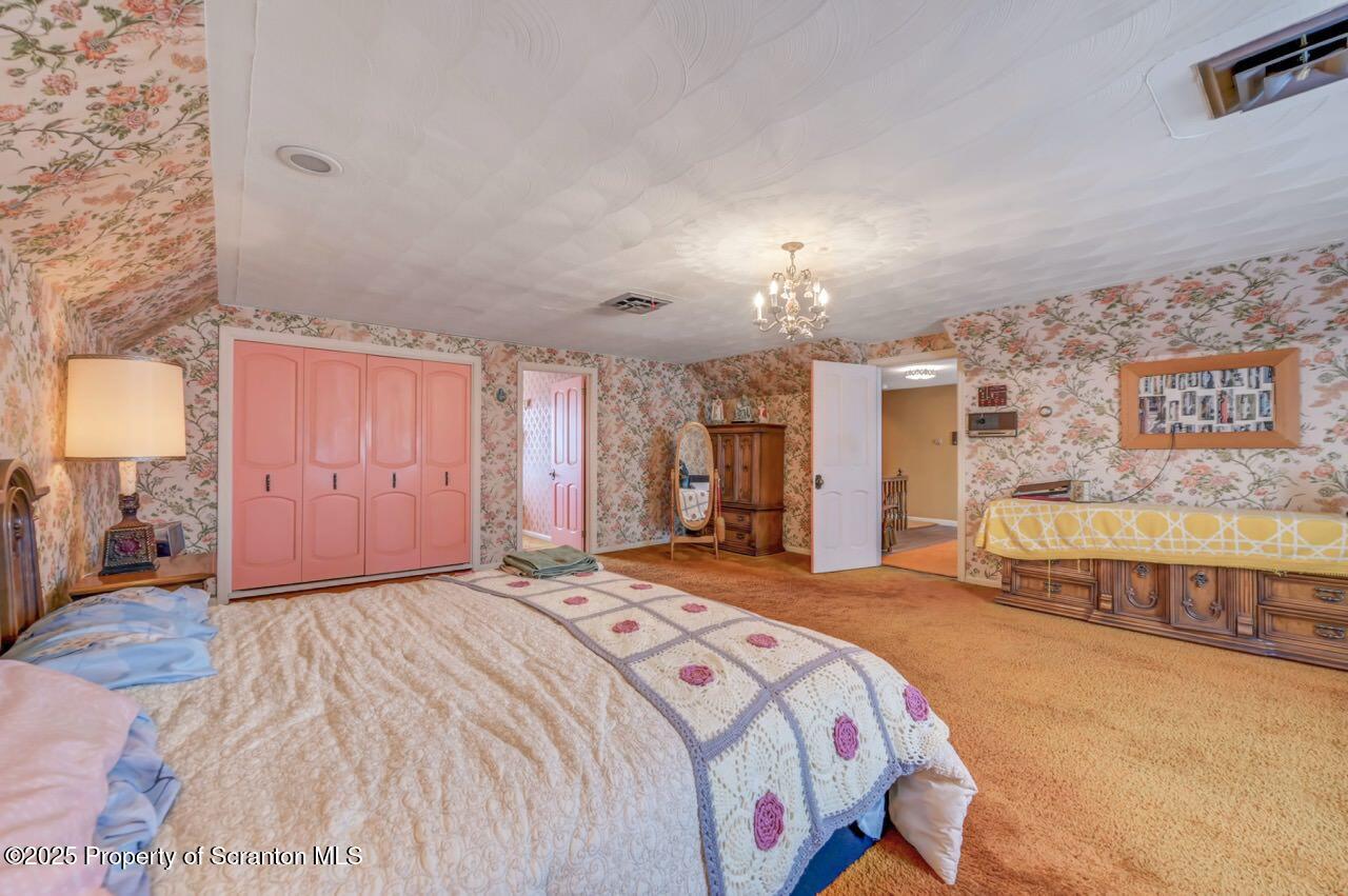 828 Glenwood Road Old Forge, PA 18518 - Photo 43 of 97 a spacious bedroom with a bed a dresser and a chandelier