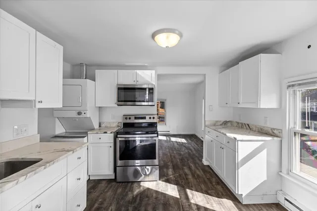 a kitchen with stainless steel appliances granite countertop a stove top oven a sink a refrigerator white cabinets and wooden floor