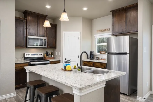 a kitchen with stainless steel appliances granite countertop a dining table chairs refrigerator and microwave