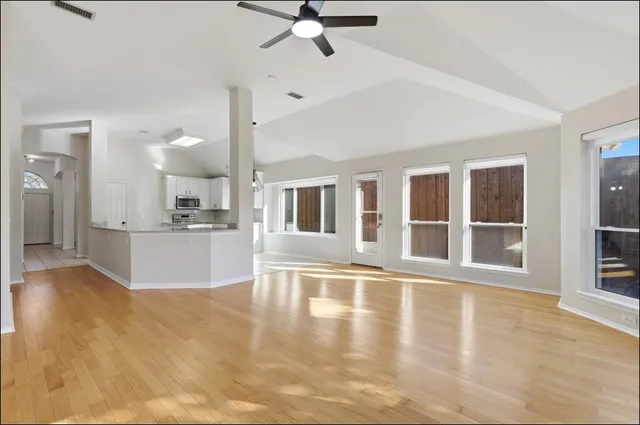 a view of an empty room with wooden floor and a kitchen