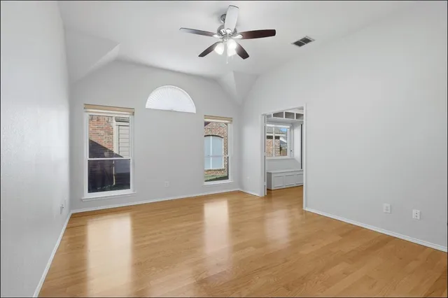 an empty room with chandelier fan and windows