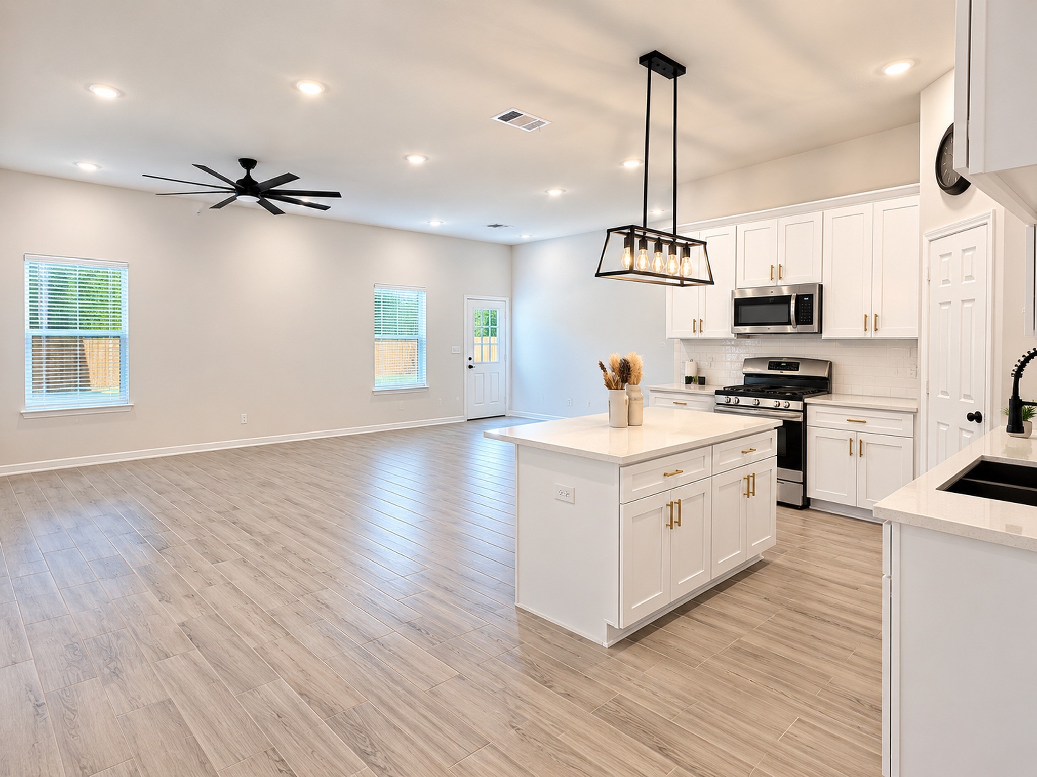 8828 Curry Road Houston, TX 77093 - Photo 3 of 15 Spacious open-concept living area with sleek wood flooring, a modern kitchen featuring stainless steel appliances, and elegant white cabinetry, all under stylish recessed lighting.