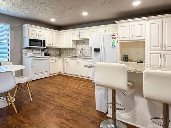 a kitchen with granite countertop a stove a sink dishwasher a refrigerator with white cabinets and wooden floor