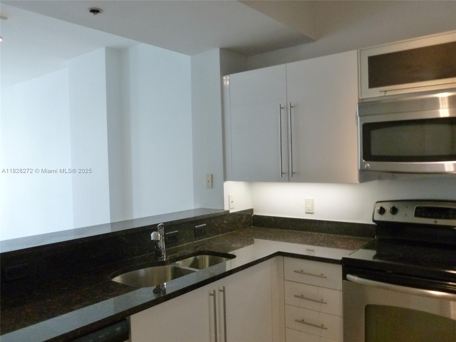 7350 Southwest 89th Street, Unit 808S Miami, FL 33156 - Photo 4 of 13 a kitchen with granite countertop white cabinets and black appliances