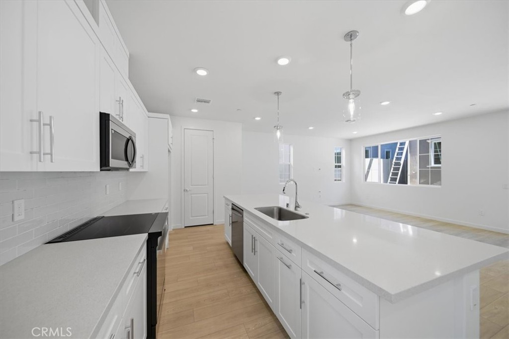 4801 Arroyo Run Moorpark, CA 93021 - Photo 10 of 27 a large white kitchen with stainless steel appliances granite countertop a sink a stove and a refrigerator with wooden floor
