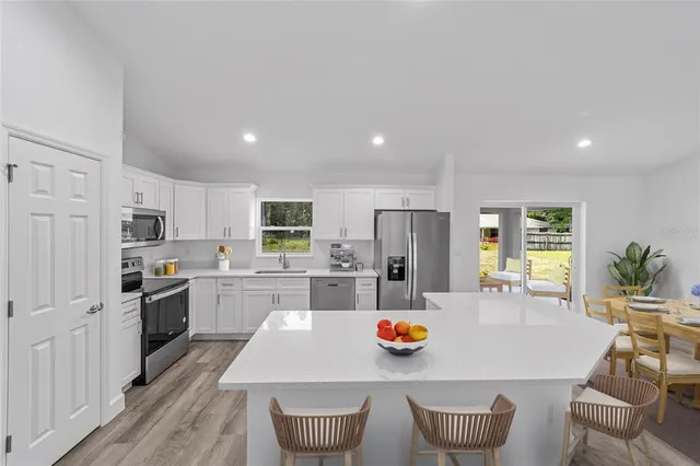 a kitchen with stainless steel appliances kitchen island granite countertop a stove a sink a refrigerator and white cabinets with wooden floor