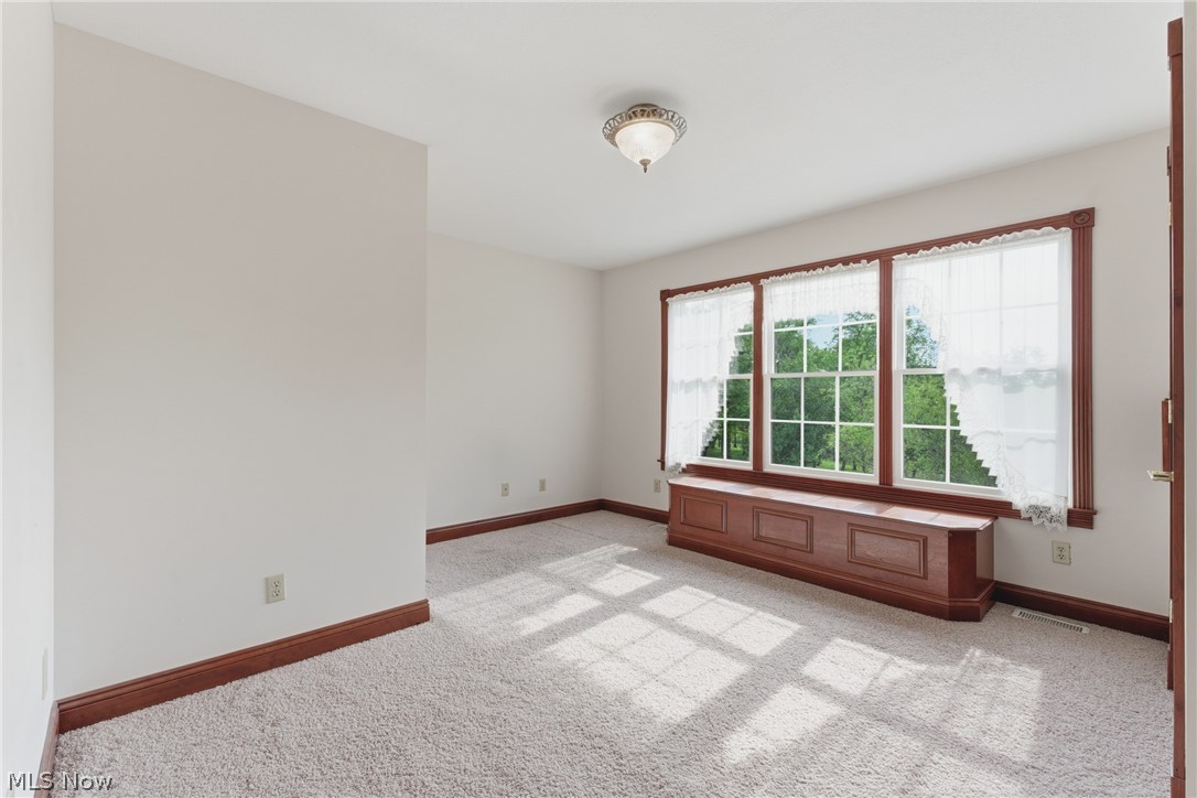 2184 Brenner Road Northeast Carrollton, OH 44615 - Photo 27 of 50 Spacious room featuring a triple window with wood trim, a built-in window seat with storage, light neutral wall paint, and light-colored carpeting