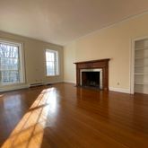 an empty room with wooden floor fireplace and windows