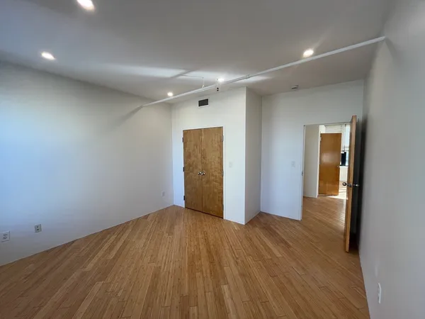 a view of an empty room with wooden floor and closet