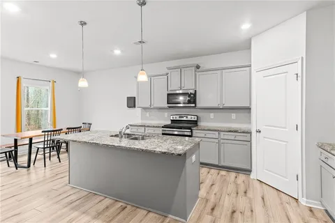 a kitchen with stainless steel appliances granite countertop a stove a sink a center island a refrigerator and a wooden floor