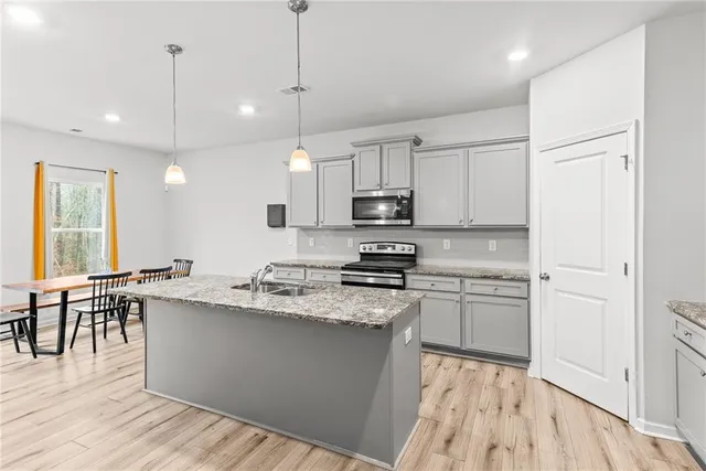 a kitchen with stainless steel appliances granite countertop a stove a sink a center island a refrigerator and a wooden floor