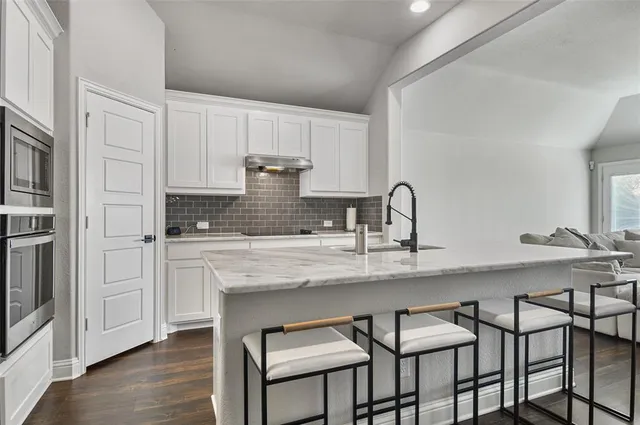 a kitchen with stainless steel appliances granite countertop a table chairs in it and white cabinets