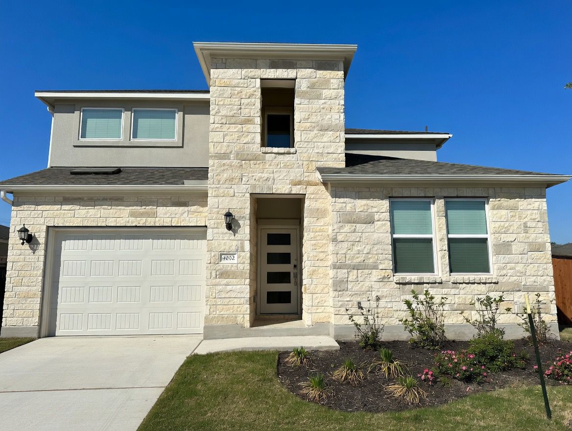 View of front facade featuring stone siding, an attached garage, driveway, and a shingled roof