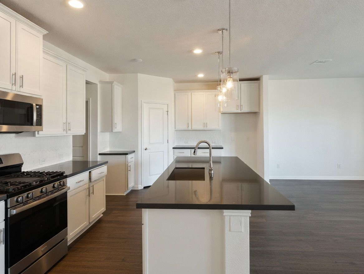 4002 Wynn Road Hutto, TX 78634 - Photo 21 of 29 Kitchen featuring stainless steel appliances, a kitchen island with sink, white cabinetry, and dark wood-type flooring