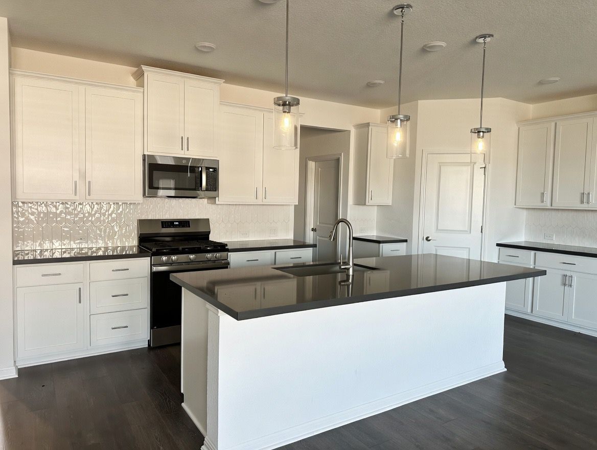 4002 Wynn Road Hutto, TX 78634 - Photo 23 of 29 Kitchen with stainless steel appliances, a center island with sink, dark wood-style floors, white cabinets, and a textured ceiling