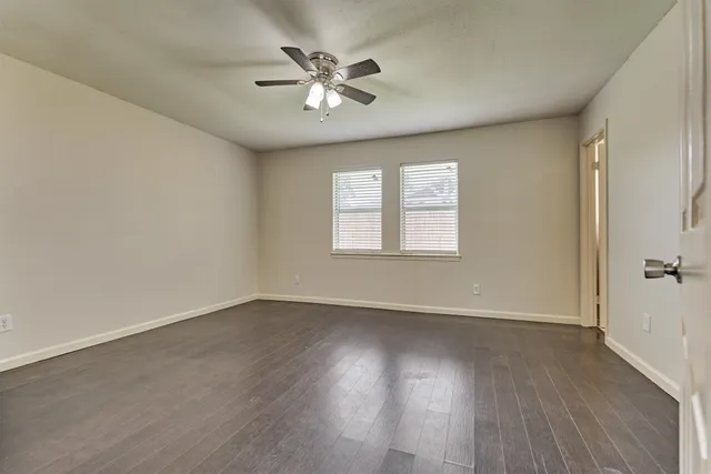 an empty room with wooden floor chandelier fan and windows
