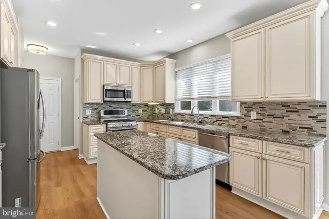 a kitchen with stainless steel appliances granite countertop a stove top oven a refrigerator a sink and dishwasher with wooden floor