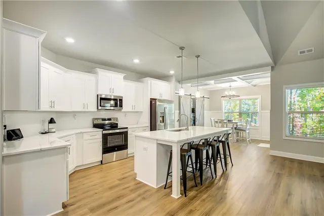 a kitchen with stainless steel appliances granite countertop a stove top oven a refrigerator a sink and white cabinets with wooden floor