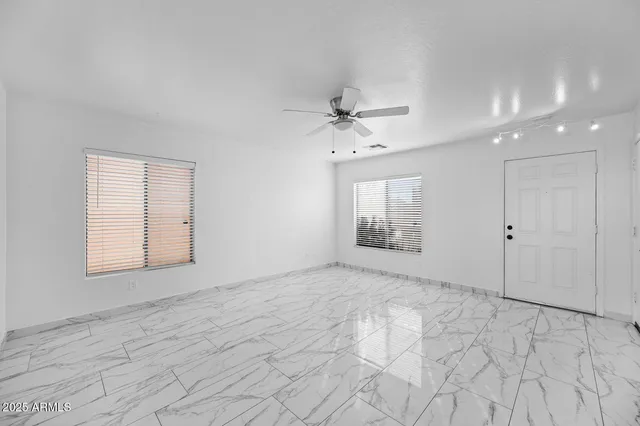 an empty room with chandelier fan and windows