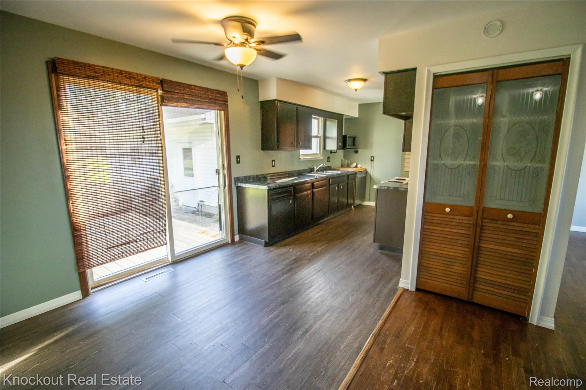 5796 East Burt Road Birch Run, MI 48415 - Photo 6 of 41 Sliding glass door with woven shades, wood-finish flooring, ceiling fan with integrated lighting, dark wood-finish cabinetry, and dark countertops