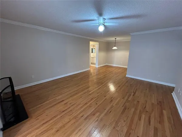 a view of an empty room with wooden floor and a ceiling fan