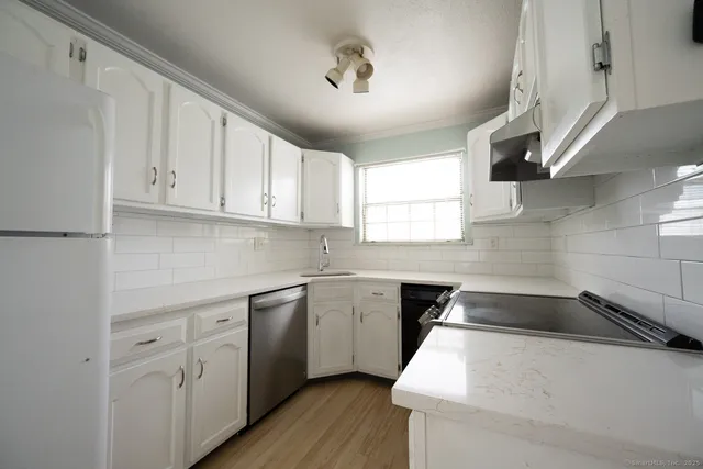 a kitchen with a sink dishwasher a stove and white cabinets with wooden floor