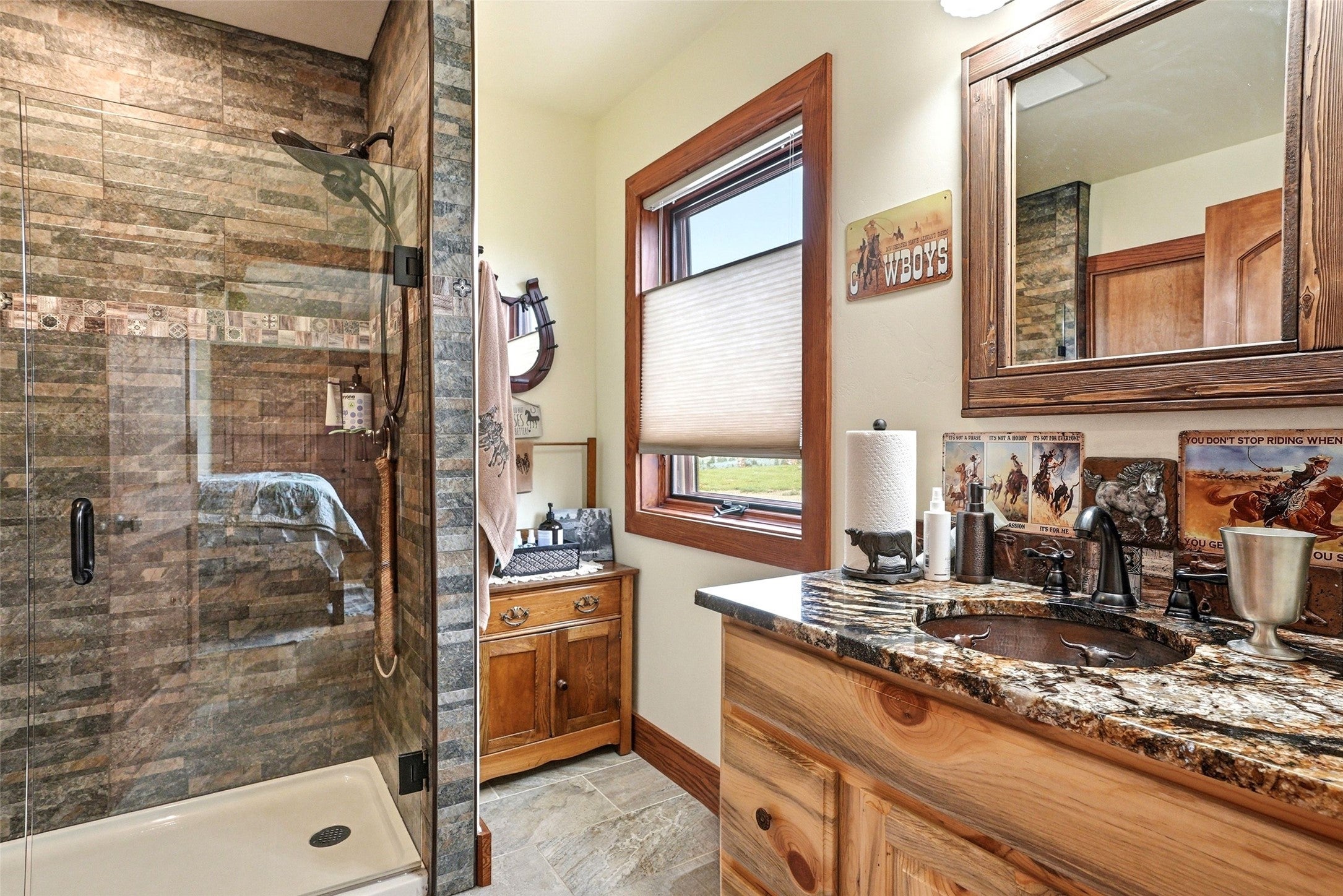 679 Hidden Valley Road North Florence, MT 59833 - Photo 30 of 85 Bathroom featuring a glass-enclosed shower with stacked stone tile, a window with cellular shades, a wood-finish vanity with a granite countertop, and a vessel sink