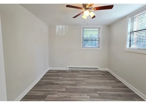 an empty room with wooden floor chandelier fan and windows
