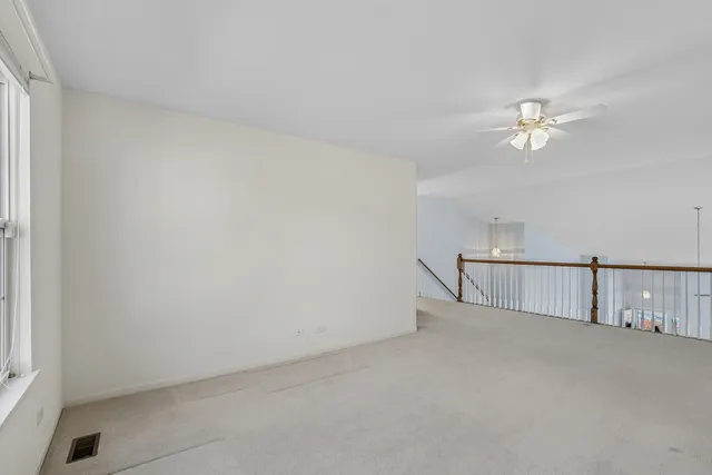 an empty room with chandelier fan and windows
