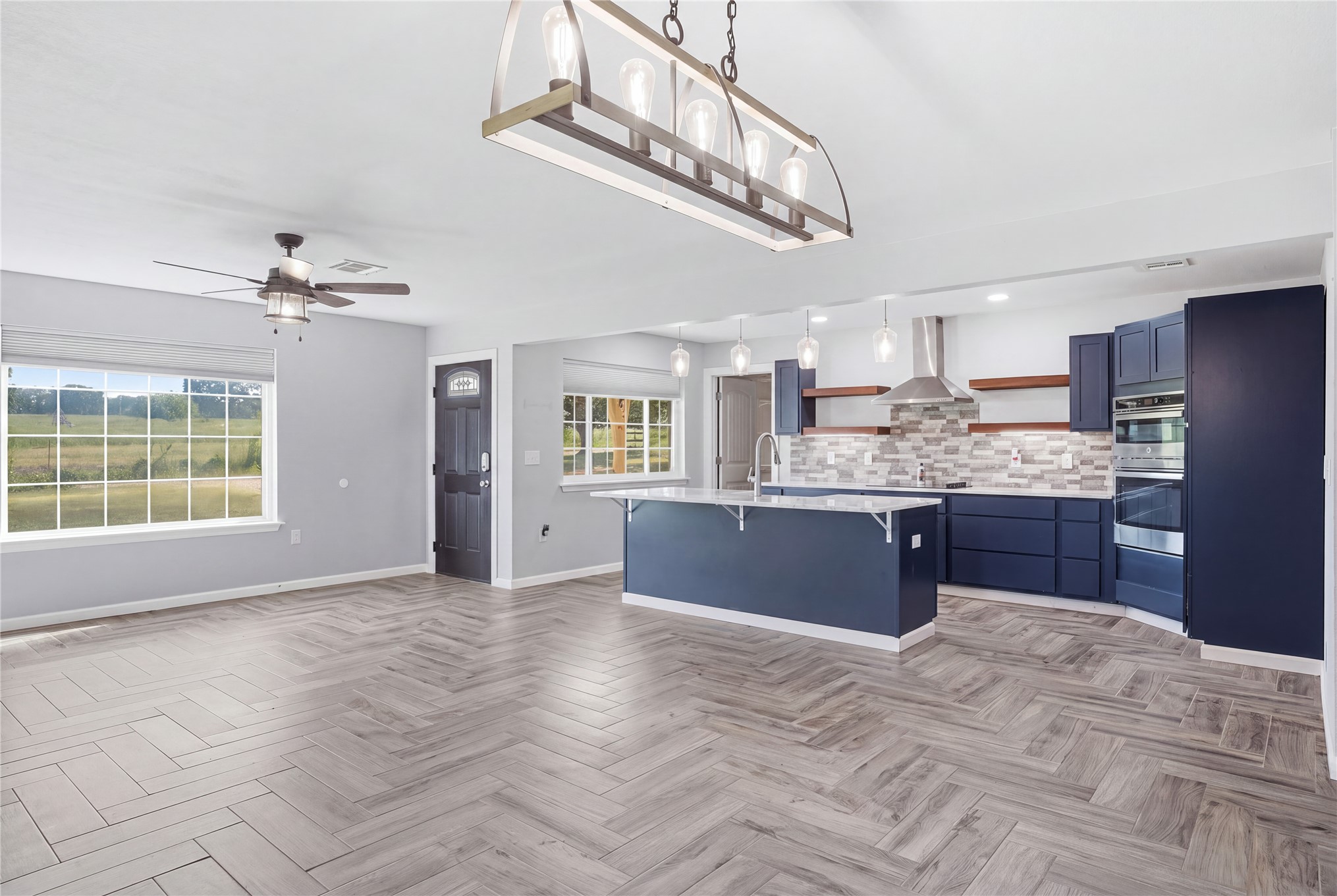 81232 South 4775 Road Stilwell, OK 74960 - Photo 22 of 50 Herringbone wood-finish flooring, custom navy cabinetry, stainless steel appliances, a kitchen island with seating, and an open-concept layout