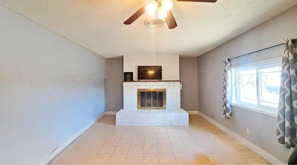 a view of a livingroom with a fireplace a ceiling fan and windows