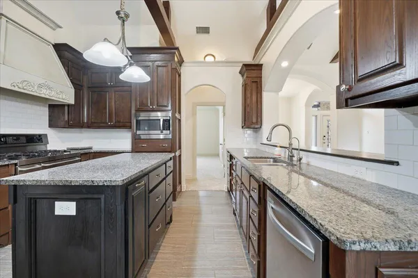 a kitchen with stainless steel appliances granite countertop a sink a stove and a wooden cabinets