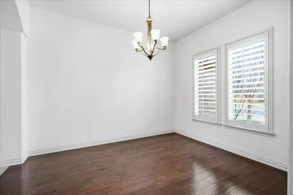 an empty room with wooden floor chandelier and windows