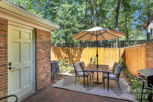 a view of a patio with a dining table and chairs under an umbrella with a small yard