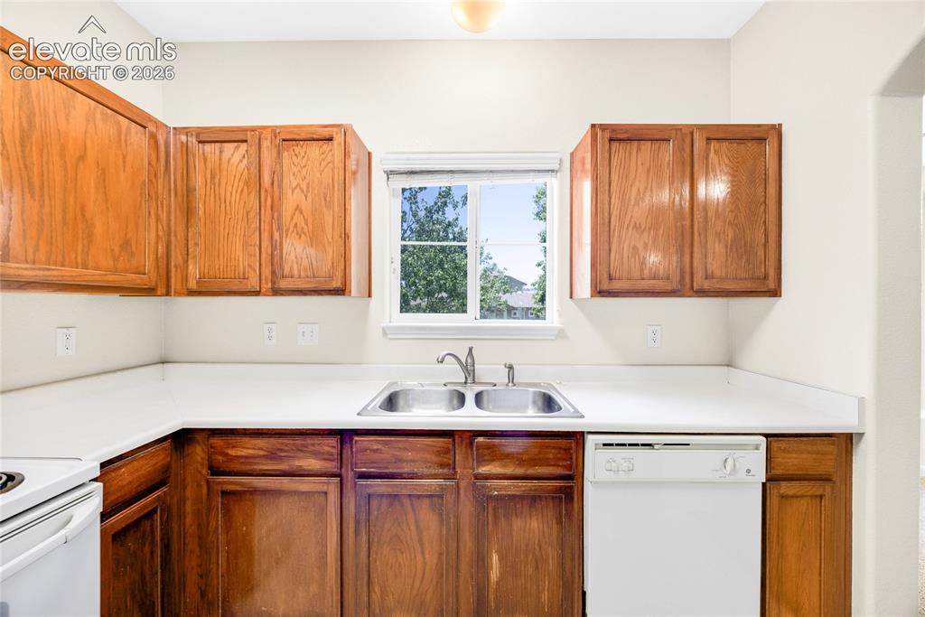 3864 Riviera Grove, Unit 102 Colorado Springs, CO 80922 - Photo 11 of 24 Kitchen featuring wood cabinetry, white countertops, a double basin stainless steel sink with a chrome faucet, a window, and a white dishwasher