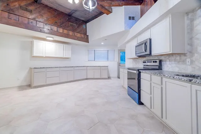 a large white kitchen with stainless steel appliances granite countertop a stove sink and cabinets