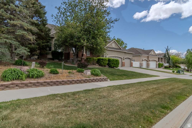 598 Hollow Creek Road Draper, UT 84020 - Photo 6 of 110 Residential streetscape showcasing a stucco and brick exterior, multi-car garage, concrete driveway, and a retaining wall with mature landscaping