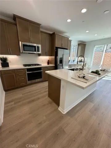 a kitchen with stainless steel appliances a stove a sink a microwave a refrigerator a refrigerator white cabinets and wooden floor