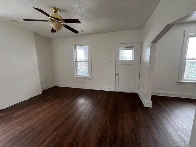 an empty room with wooden floor chandelier fan and windows