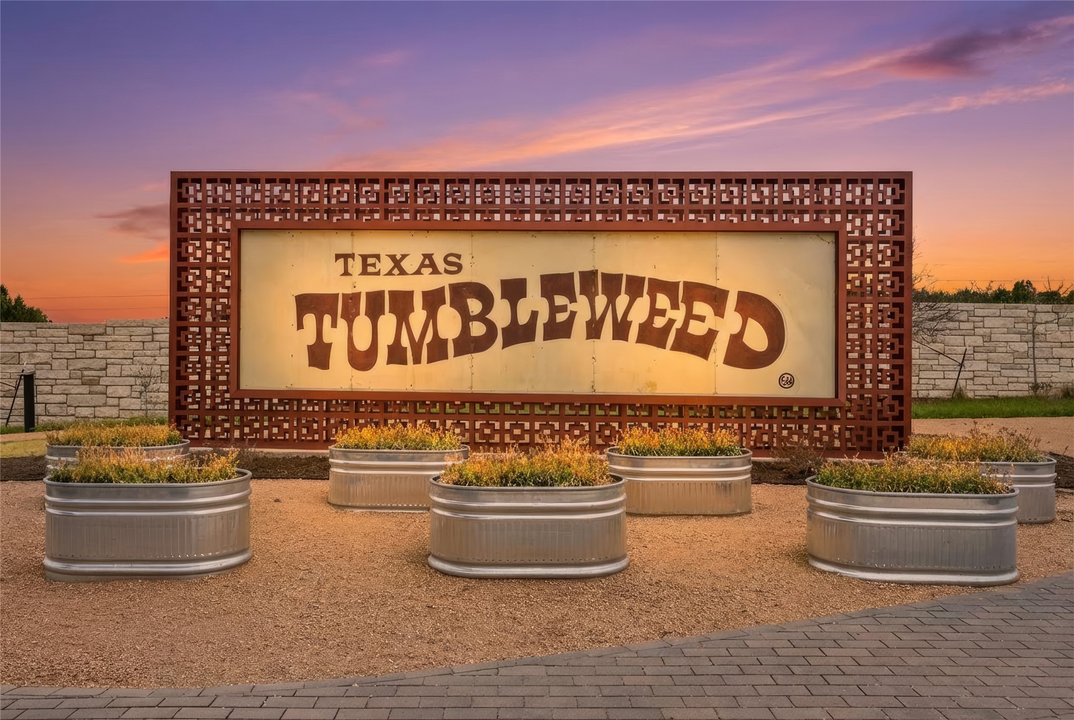 9803 Ribelin Ranch Court, Unit 21 Austin, TX 78750 - Photo 16 of 20 Community entrance featuring a decorative sign, multiple planted metal containers, and a stone wall