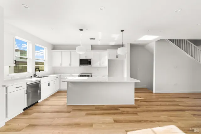 a large white kitchen with kitchen island a sink white cabinets and stainless steel appliances