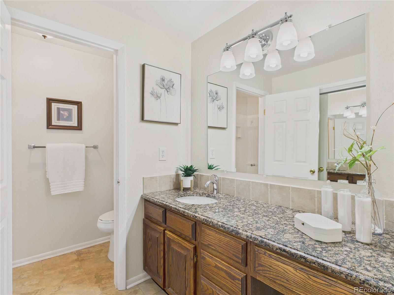 8373 Zephyr Street Arvada, CO 80005 - Photo 11 of 31 a bathroom with a granite countertop sink a toilet and a large mirror
