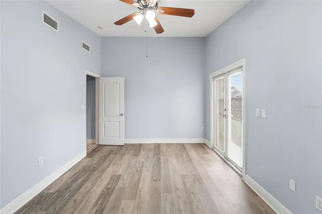 an empty room with wooden floor fan and windows