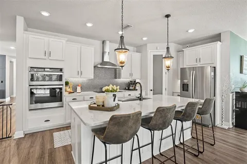 a kitchen with stainless steel appliances kitchen island granite countertop a refrigerator a stove a microwave oven a sink with island chairs and wooden floor