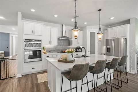 a kitchen with stainless steel appliances kitchen island granite countertop a refrigerator a oven a sink a island and chairs with wooden floor