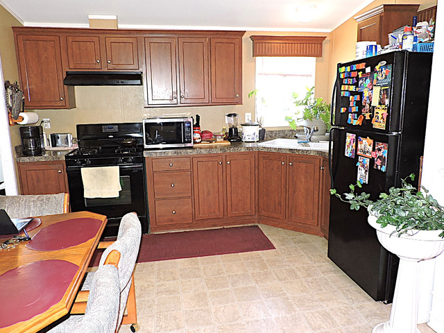 915 North 5000 W Road Hinckley, UT 84635 - Photo 9 of 27 Kitchen featuring wood-finish cabinetry, black appliances, a corner sink with a window, and durable flooring