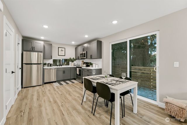 a open kitchen with stainless steel appliances granite countertop a refrigerator a stove a sink dishwasher a dining table and chairs with wooden floor