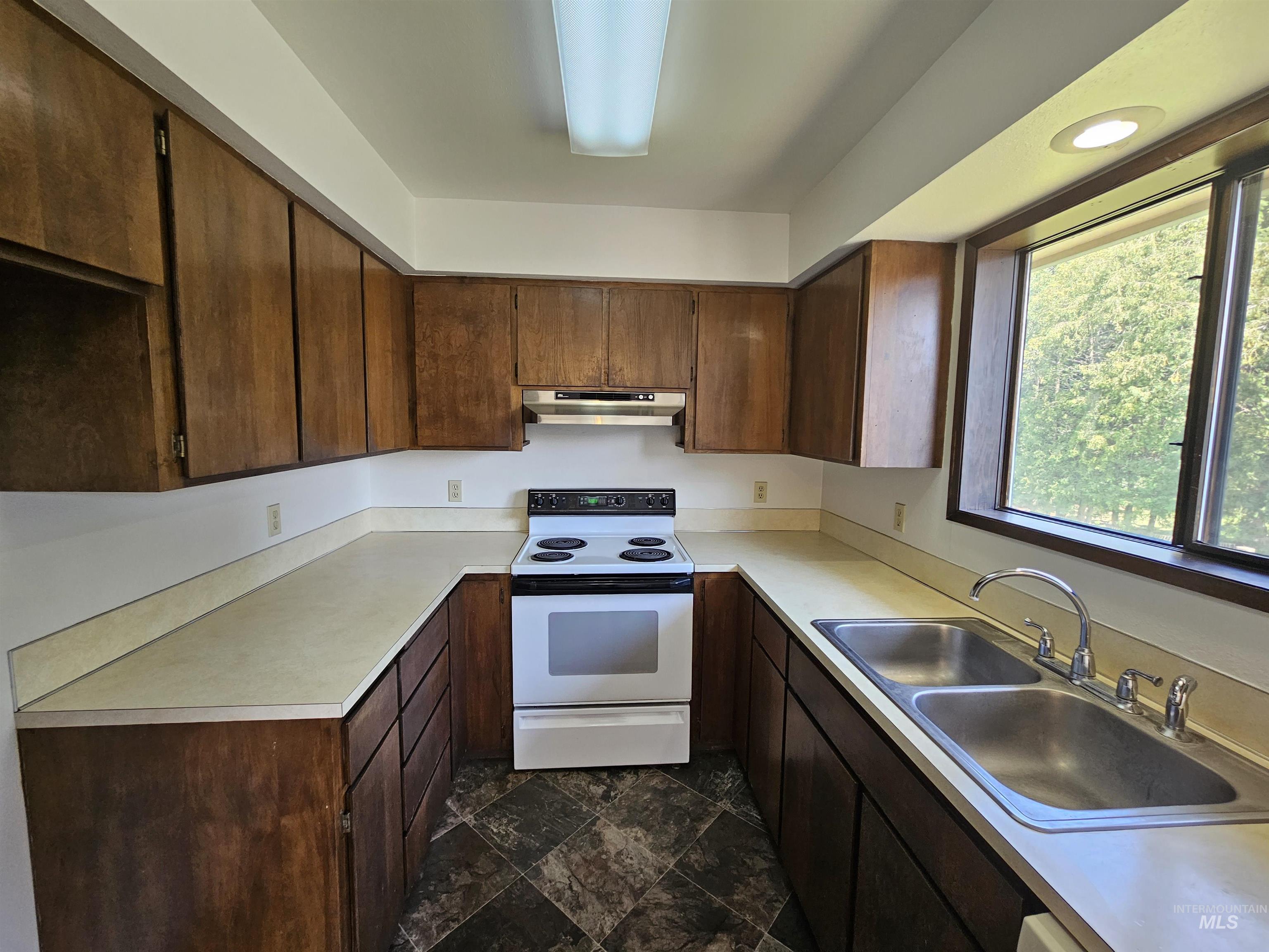 1825 Cedar Avenue Lewiston, ID 83501 - Photo 7 of 39 Kitchen with white electric stove, light countertops, dark brown cabinets, under cabinet range hood, and dark stone finish flooring